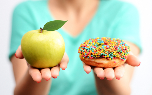 Mujer con manzana verde en una mano y una donnut en la otra mano 