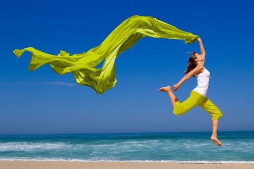 Mujer saltando con pañuelo verde frente al mar